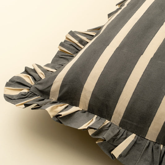 A close-up of a striped pillow with a ruffled edge, featuring alternating dark gray and beige vertical stripes on a light cream background.