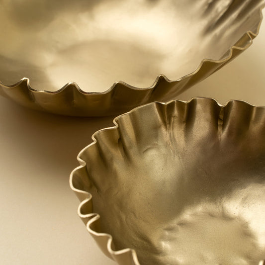 Two metallic gold fluted bowls with a hammered texture, shown in a close-up studio shot on a neutral beige background.