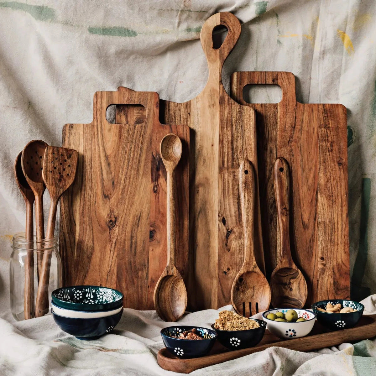 Set of wooden cutting boards and spoons on a textured fabric background.