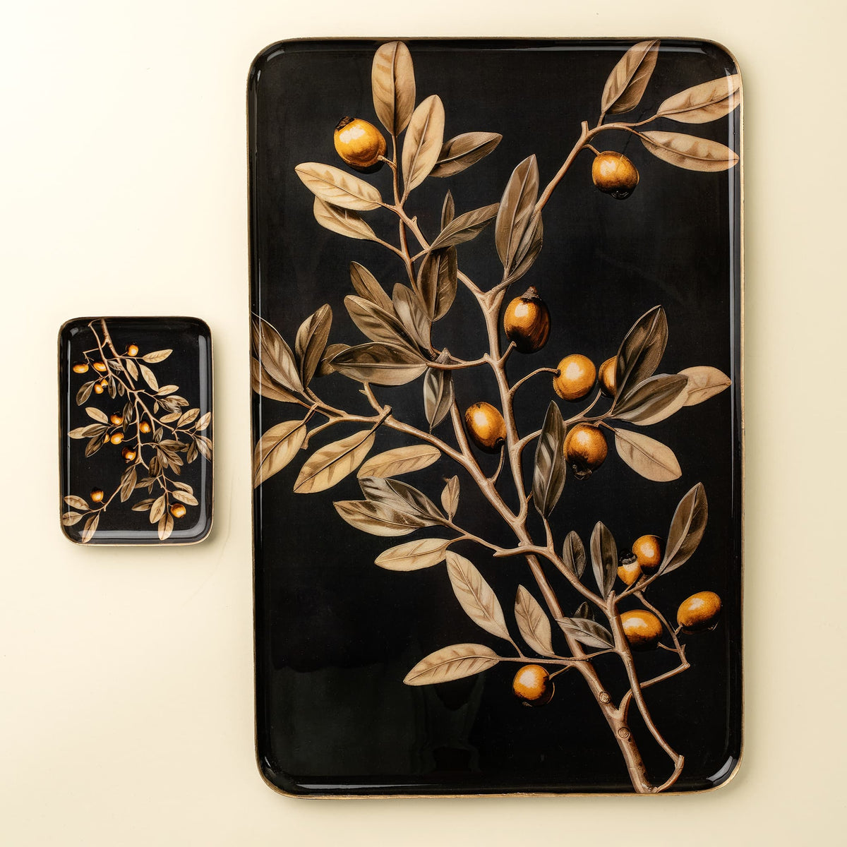 A rectangular black tray with a glossy finish featuring a botanical illustration of a branch with brown leaves and small orange-brown fruits, shown alongside a smaller matching square tray on a light beige background.