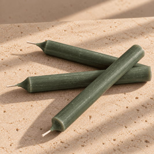 Three pine green taper candles arranged in a crossed pattern on a textured beige stone surface with soft diagonal shadows.