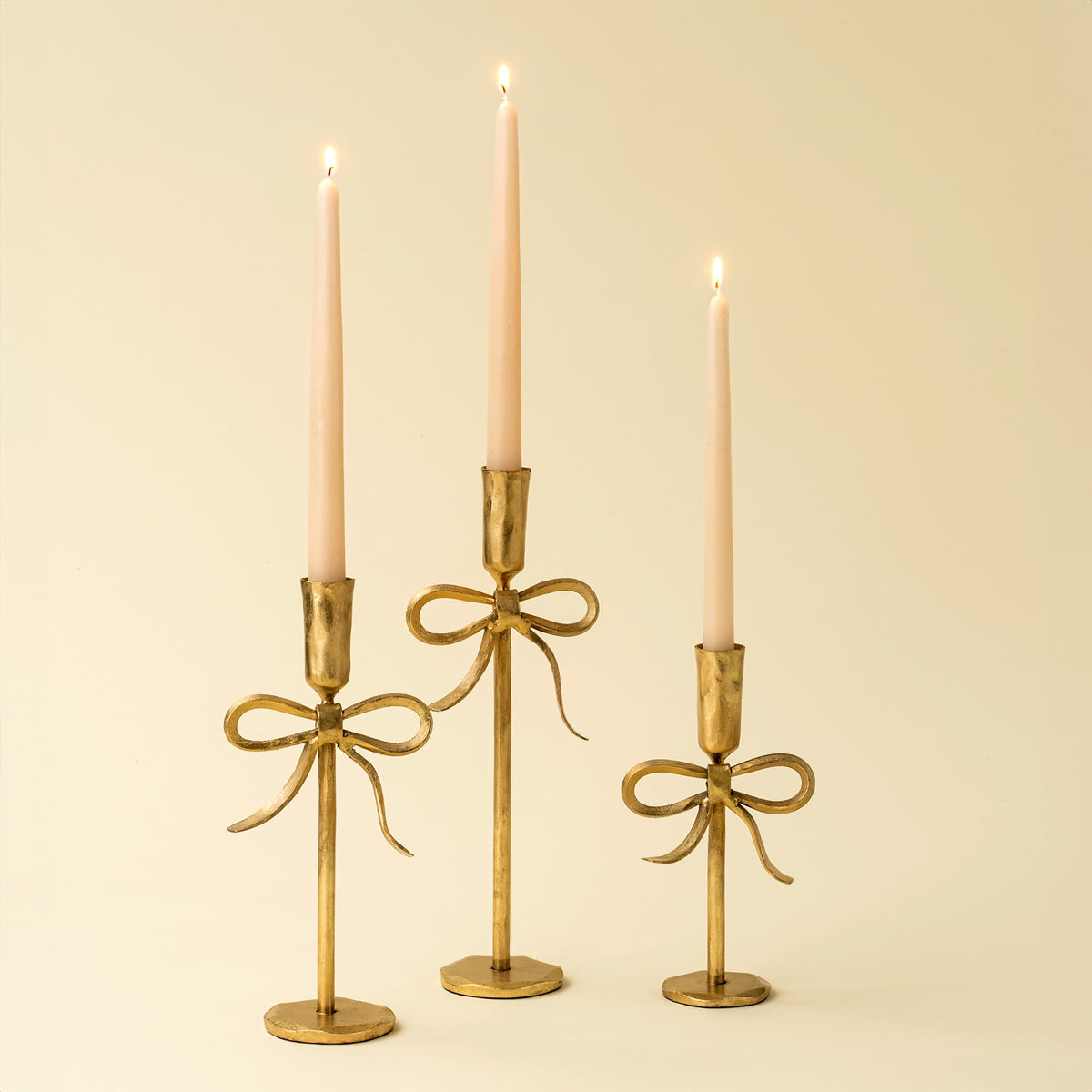 Three gold candle holders with candles on a beige background.