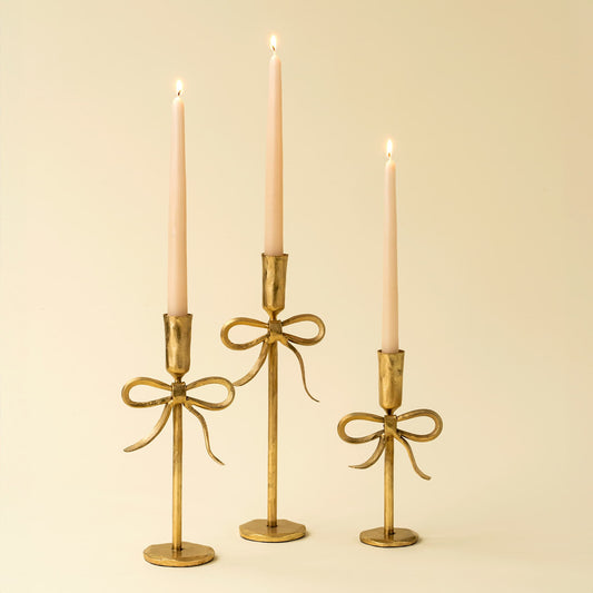 Three gold candle holders with candles on a beige background.