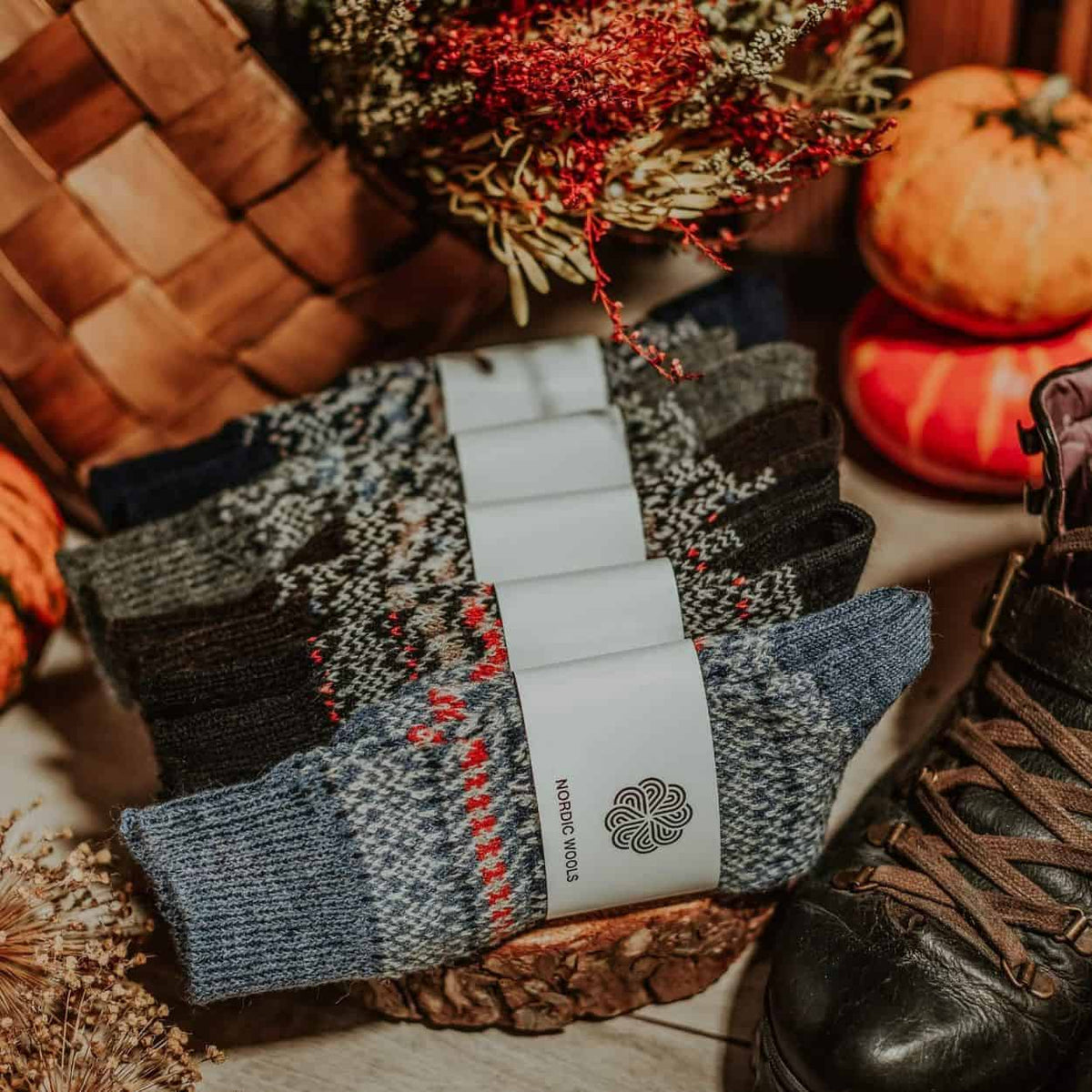 Pair of patterned socks with a brand label on a rustic background with pumpkins and a woven basket.