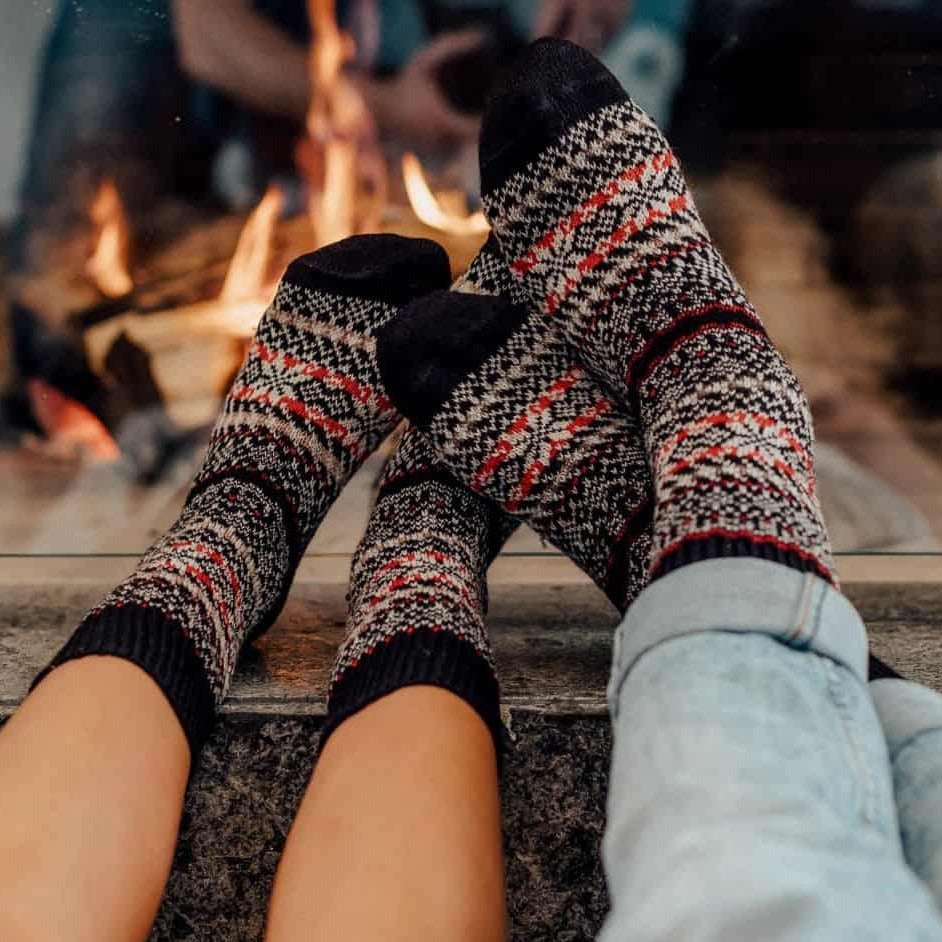 Two pairs of feet wearing patterned socks by a fireplace.