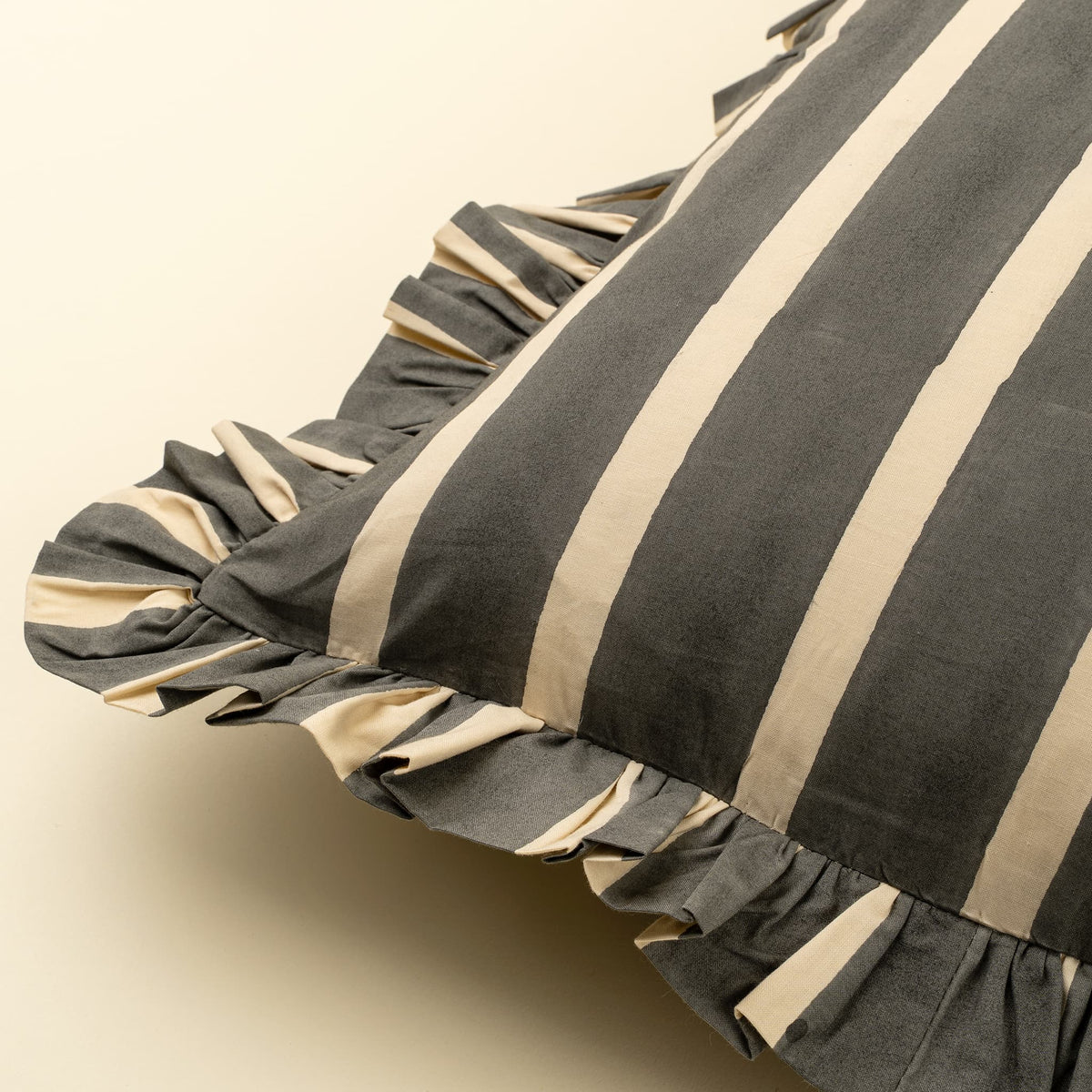 A close-up of a striped pillow with a ruffled edge, featuring alternating dark gray and beige vertical stripes on a light cream background.