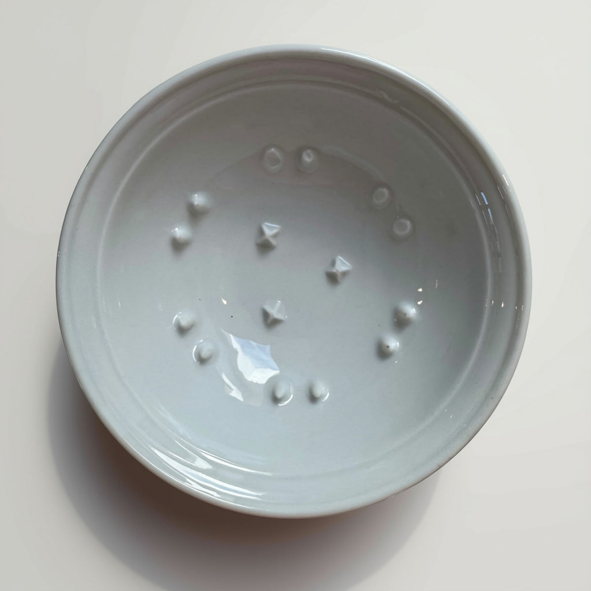 A white ceramic grapefuit bowl with prong pattern, photographed from directly above on a light beige surface.