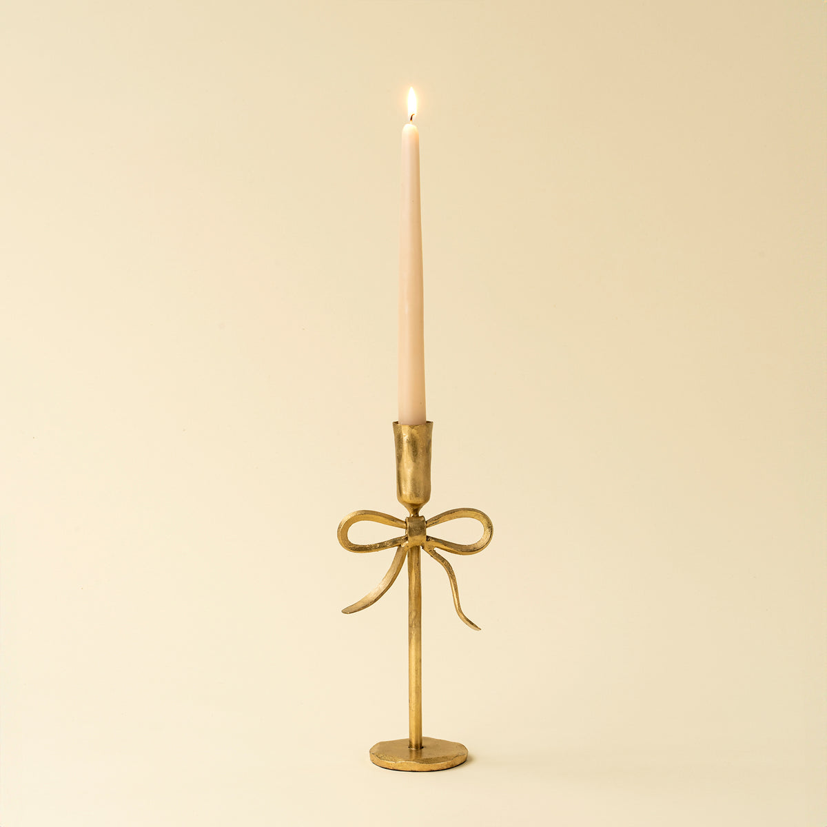Gold candle holder with a bow design on a beige background.