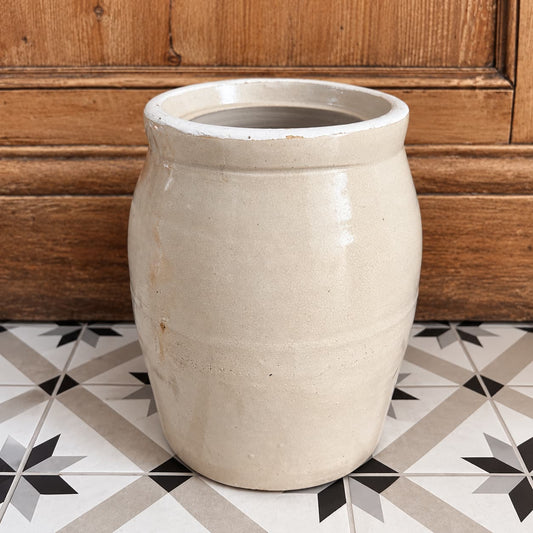 Antique cream-coloured stoneware pot on a patterned tile floor with an old barn wood background.
