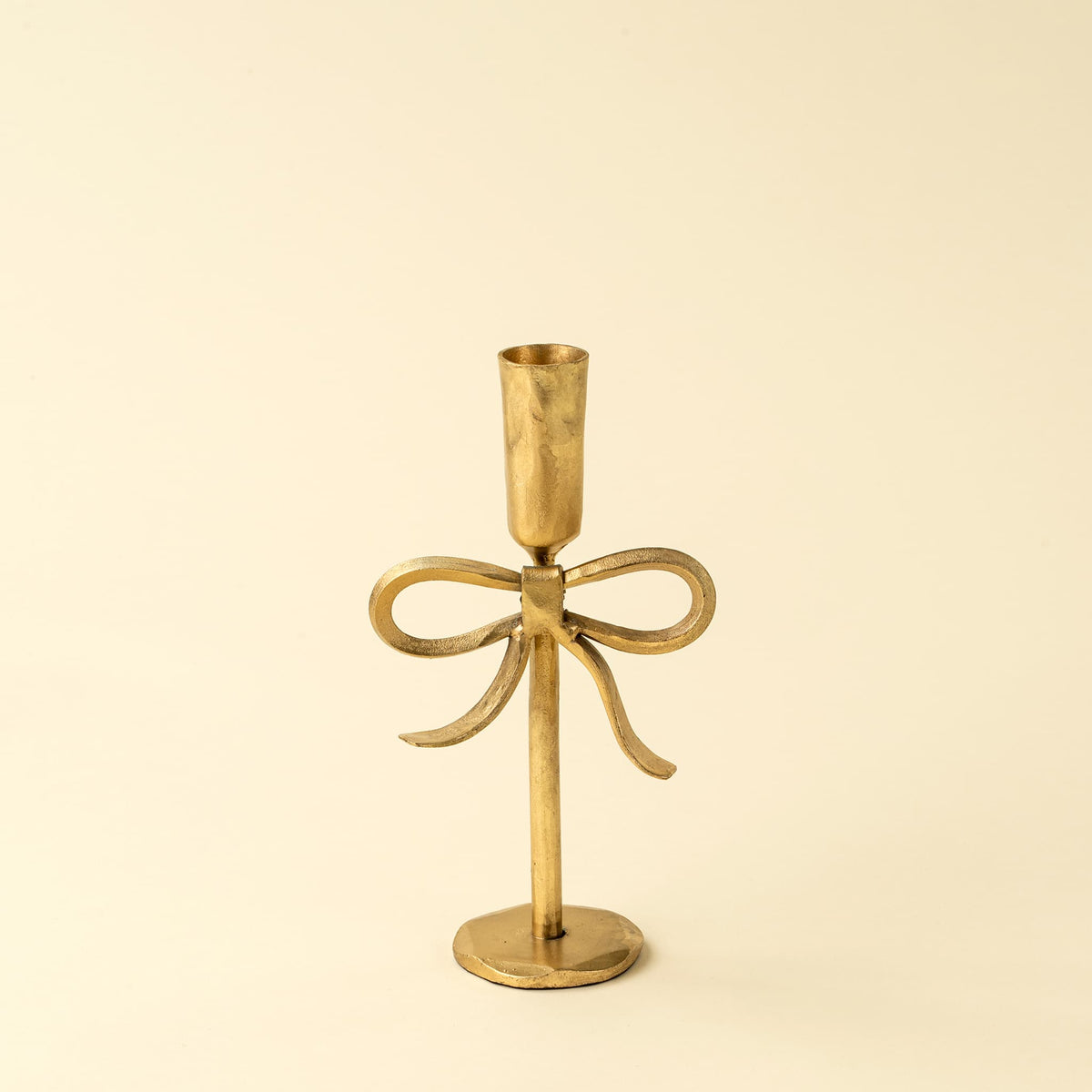 A small brass bow-shaped candlestick holder, set against a solid cream background.