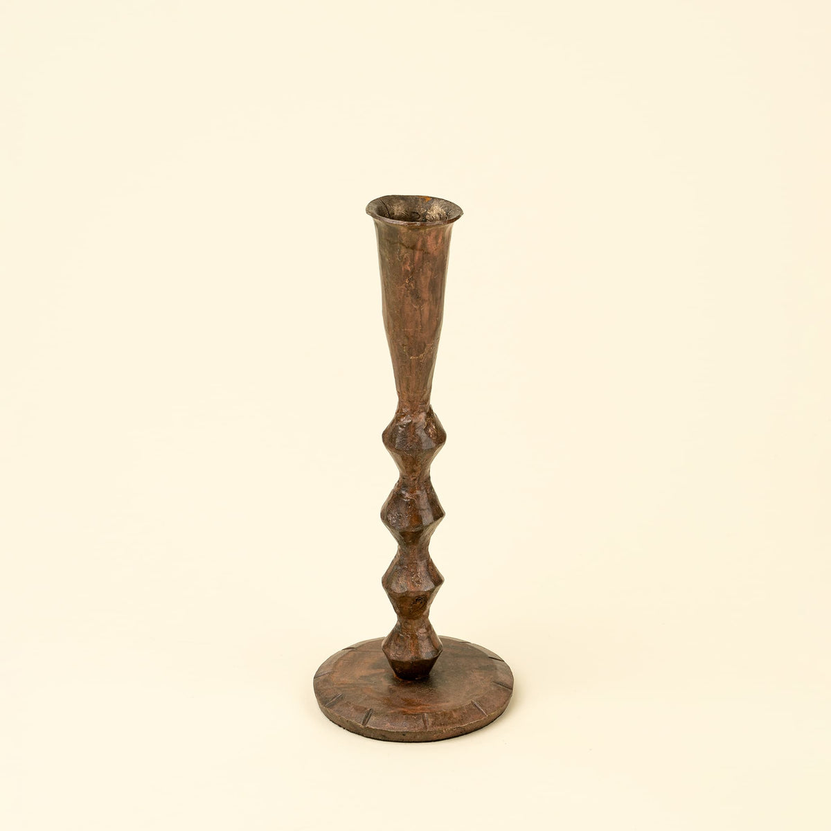 A rustic, dark brown wooden candlestick with a flared rim top and a round base, featuring a series of knurled, bulbous details down the stem, set against a solid cream background.