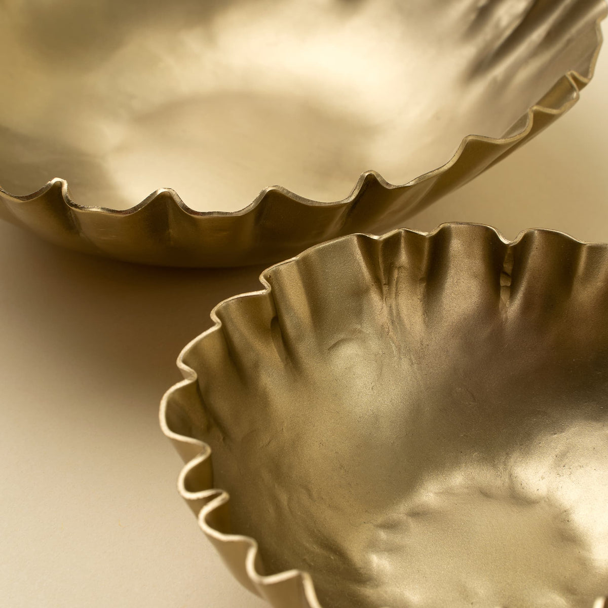 Two metallic gold fluted bowls with a hammered texture, shown in a close-up studio shot on a neutral beige background.