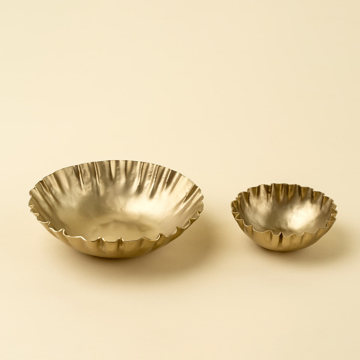 Two metallic gold fluted bowls, one large and one small, displayed on a warm beige background.