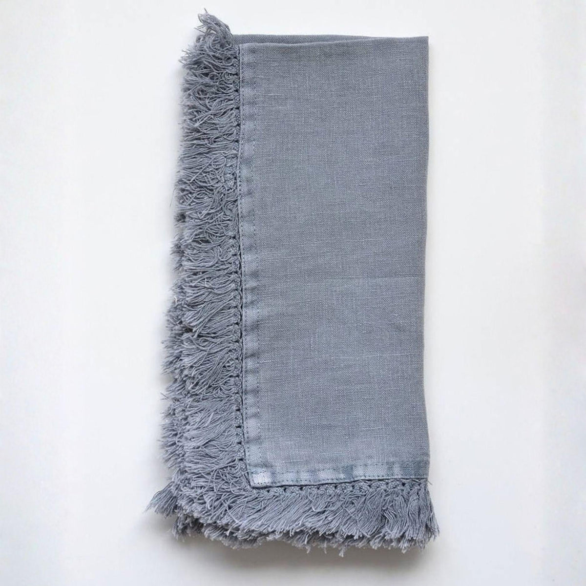 A folded light gray linen napkin with fringed edges, displayed flat against a clean white background.