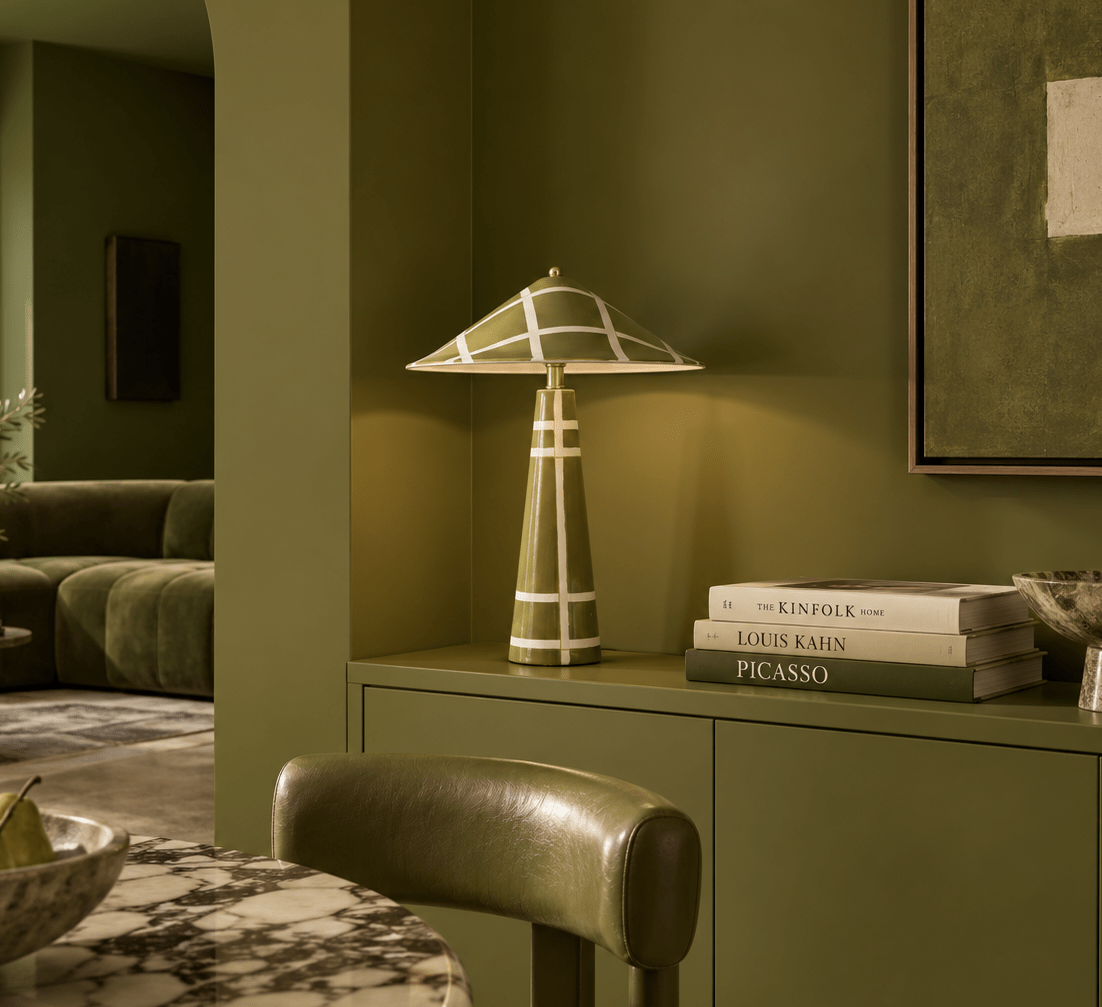 A sculptural olive green ceramic table lamp, styled on a matching olive green console table in a modern living room setting.