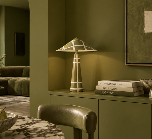 A sculptural olive green ceramic table lamp, styled on a matching olive green console table in a modern living room setting.