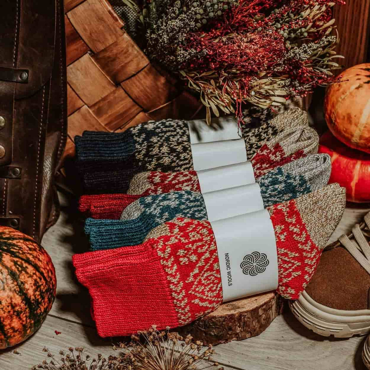 Set of patterned socks with a brand label on a wooden surface, surrounded by autumn-themed decor.