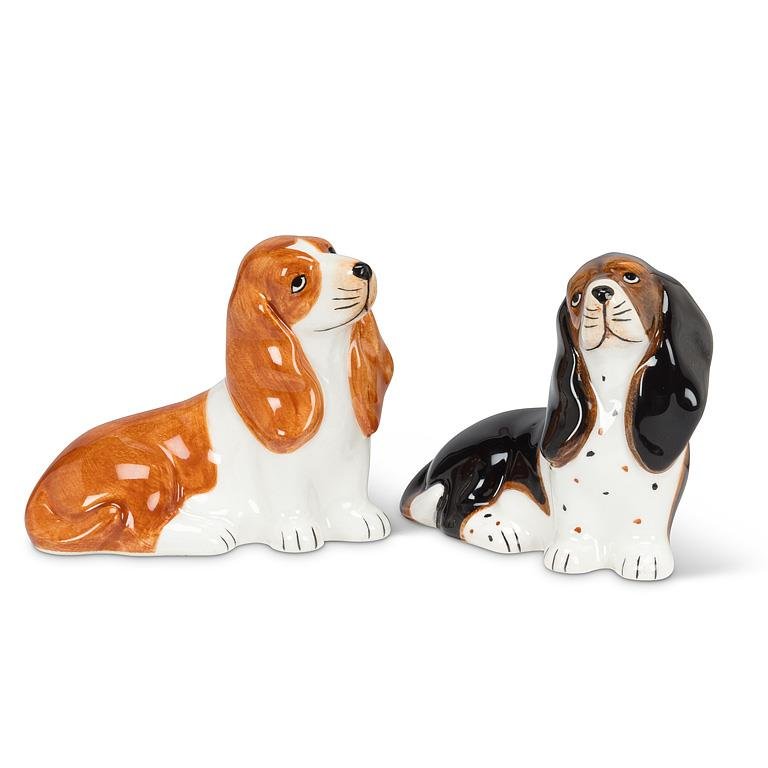 Two ceramic basset hound salt and pepper shakers on a plain white background, one in brown and white and one in black and white with brown spots.
