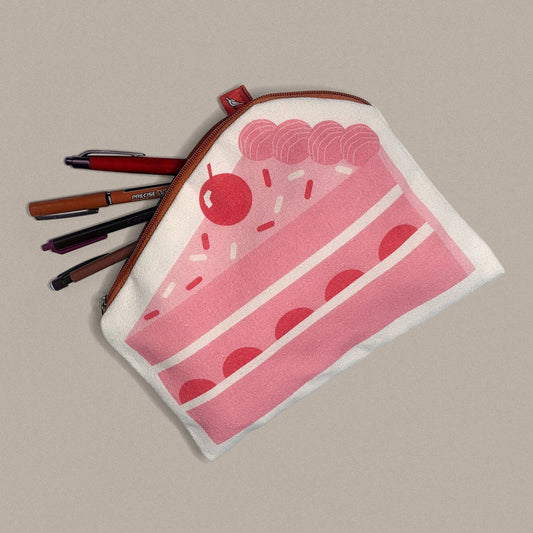 A fabric zippered pouch with a pink slice-of-cake illustration and a cherry, shown on a plain taupe background with several pens tucked inside.