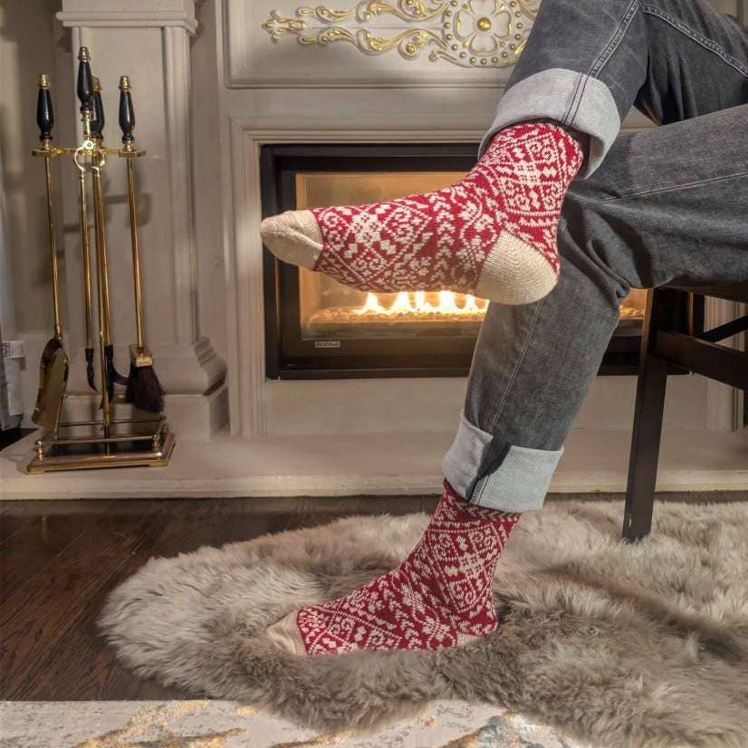Person wearing red patterned socks sitting by a fireplace with Christmas decorations.