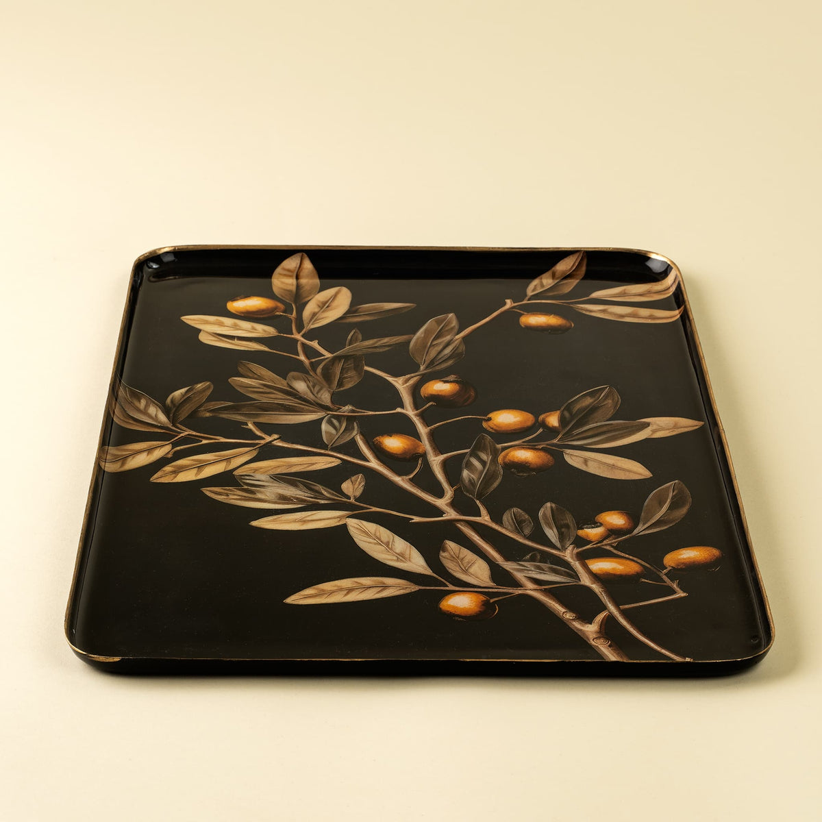 Black enamel decorative tray with olive branch design on a beige background.