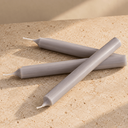 Three pale grey taper candles arranged in an X pattern on a textured beige stone surface with soft shadows.