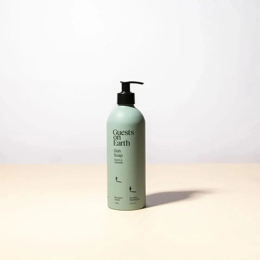 Green bottle of 'Guests on Earth' dish soap on a beige surface with a white background