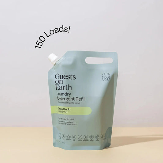 Guests on Earth Laundry Detergent Refill pouch in Green Hinoki on a light beige surface against a light gray background, with a black curved text overlay reading '150 Loads!'.