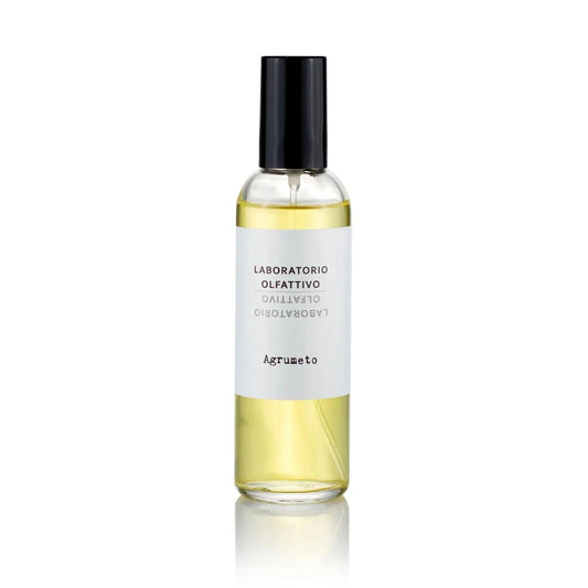 A clear glass spray bottle filled with pale yellow liquid, featuring a white label with black text and a black spray cap, centered on a white background with a soft reflection below.