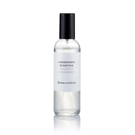 A clear glass spray bottle filled with clear liquid, featuring a white label with black text and a black spray cap, centered on a white background with a soft reflection below.