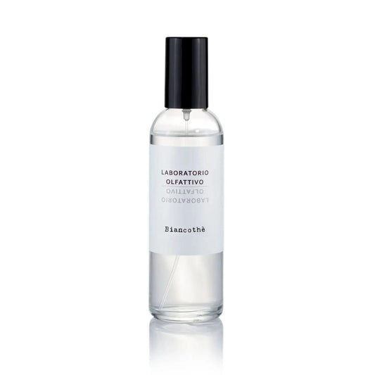 A clear glass spray bottle filled with clear liquid, featuring a white label with black text and a black spray cap, centered on a white background with a soft reflection below.