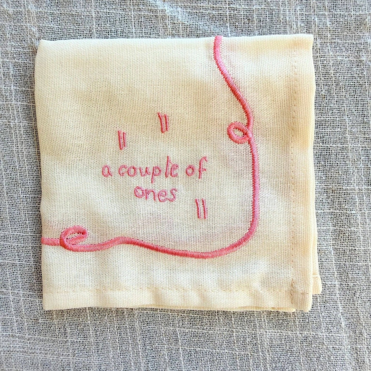 Embroidered fabric square with 'a couple of ones' text on a textured surface.