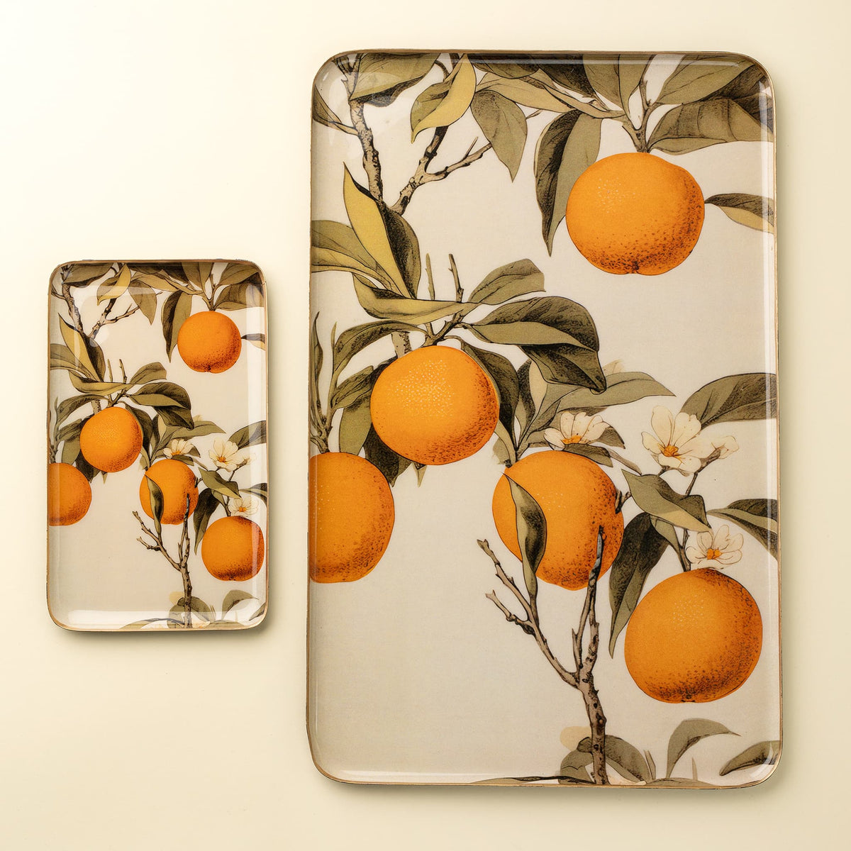 Two rectangular decorative trays with rounded corners, featuring a vintage-style botanical print of oranges on branches with green leaves and white flowers, set against a warm cream background.