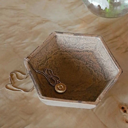 Hexagonal jewelry dish with a necklace on a wooden surface with flowers in the background.