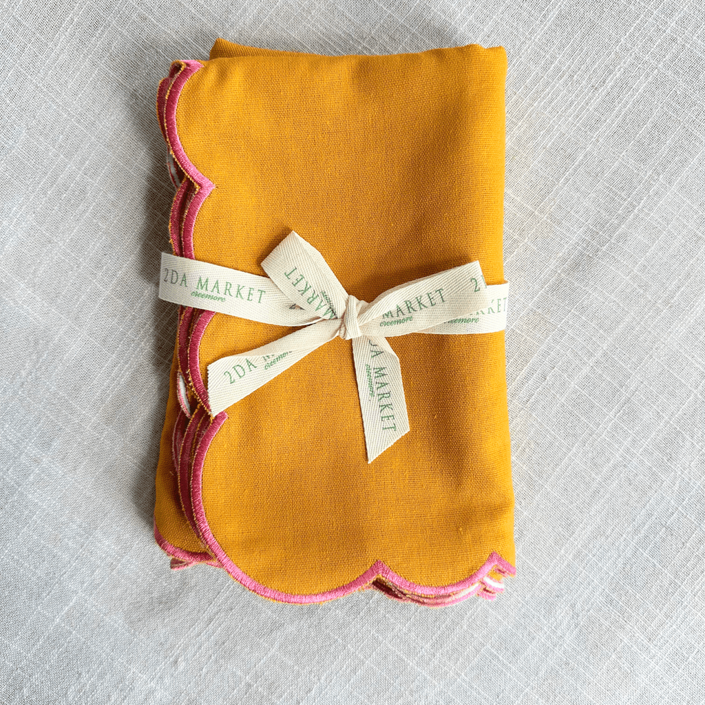 A folded mustard yellow fabric napkin with pink scalloped edges, tied with a cream ribbon.