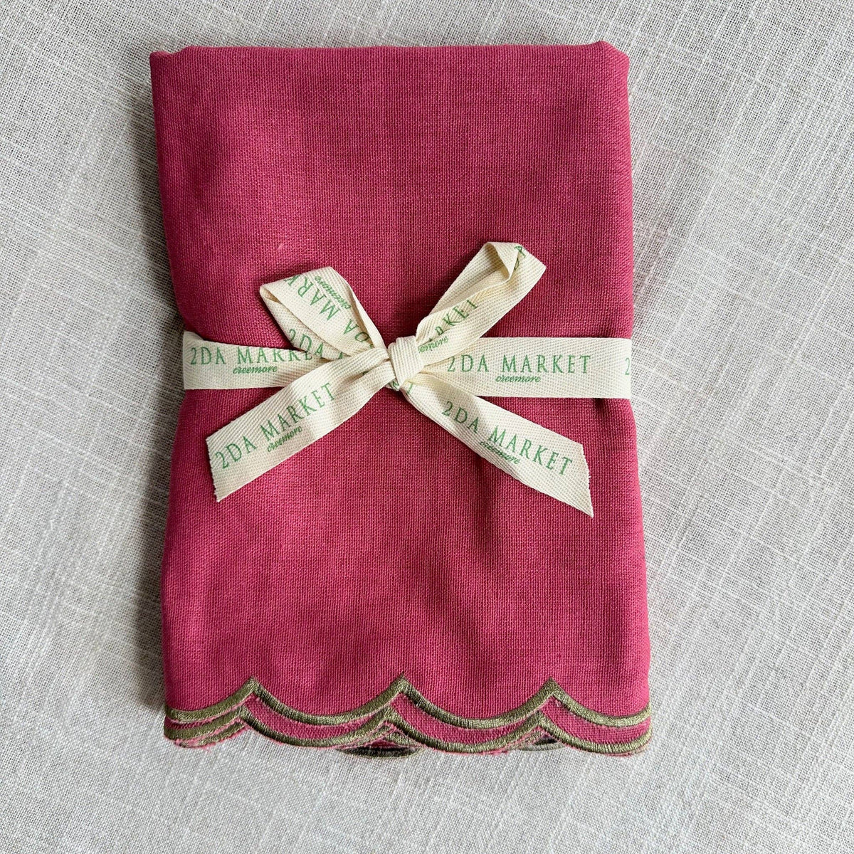 A folded magenta pink linen napkin with a scalloped edge, tied with a cream ribbon.