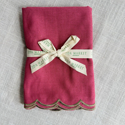 A folded magenta pink linen napkin with a scalloped edge, tied with a cream ribbon.