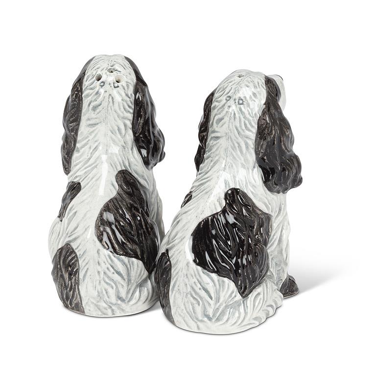 A pair of ceramic salt and pepper shakers shaped like black and white spaniel dogs, shown from the back on a white background.